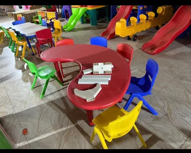 Red children’s plastic table with green, blue and yellow chairs, with slides behind it