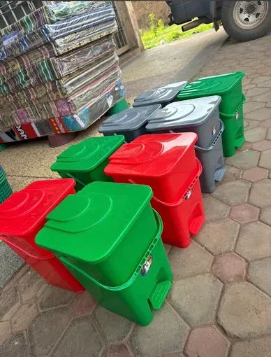 Green, red and grey plastic pedal bins with closed lids, lined up outside the shop